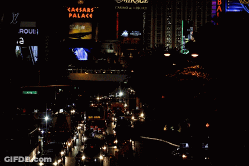 A Busy City Street At Night With A Sign For The Caesars Palace In The Background GIF