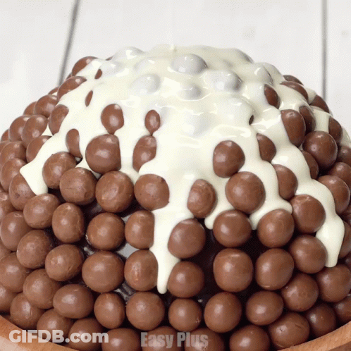 A Cake Covered In Chocolate Balls And White Frosting With Easy Plus On The Bottom GIF