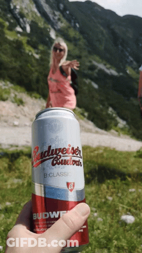 A Can Of Budweiser Is Being Held Up In Front Of A Mountain GIF