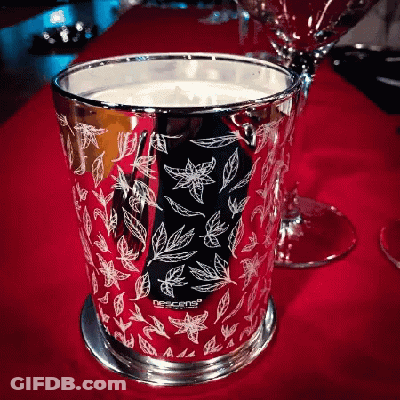 A Candle In A Silver Cup With Leaves On It Is On A Red Table GIF