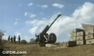 A Cannon Is Being Fired In A Field With Boxes In The Background . GIF