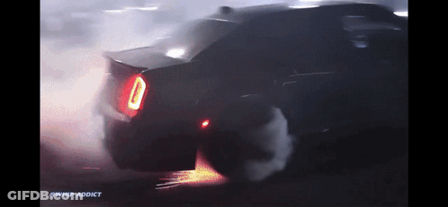 A Car Is Doing A Burnout In The Dark With Smoke Coming Out Of The Tire GIF