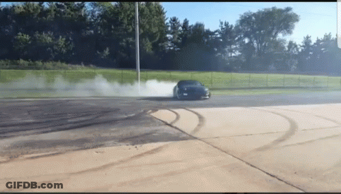 A Car Is Drifting In A Parking Lot With Smoke Coming Out Of The Tire GIF