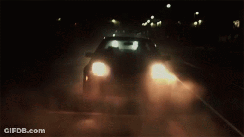 A Car Is Driving Down A Dark Road At Night With Its Headlights On . GIF