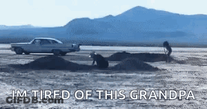 A Car Is Driving Down A Dirt Road Next To A Pile Of Dirt And Mountains . GIF