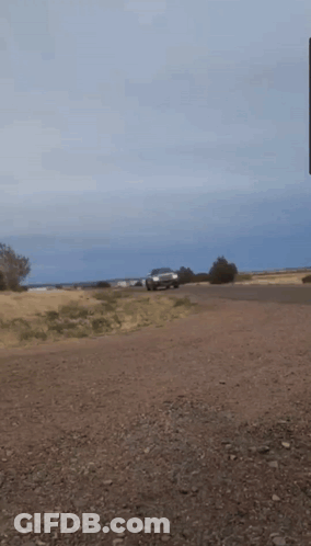 A Car Is Driving Down A Dirt Road With A Blue Sky In The Background GIF