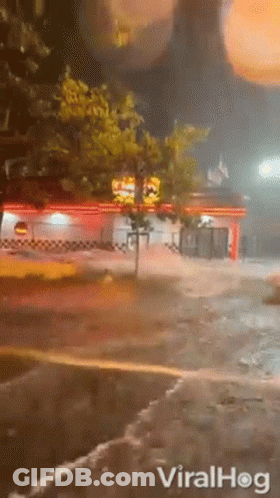 A Car Is Driving Down A Flooded Street At Night In Front Of A Restaurant . GIF