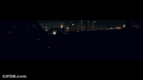 A Car Is Driving Down A Highway At Night With A Reflection Of A Building In The Background GIF