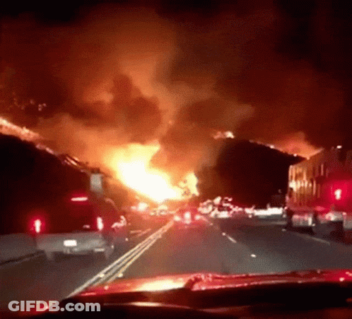 A Car Is Driving Down A Highway In Front Of A Huge Fire GIF