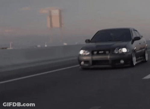 A Car Is Driving Down A Highway With A Bridge Behind It GIF