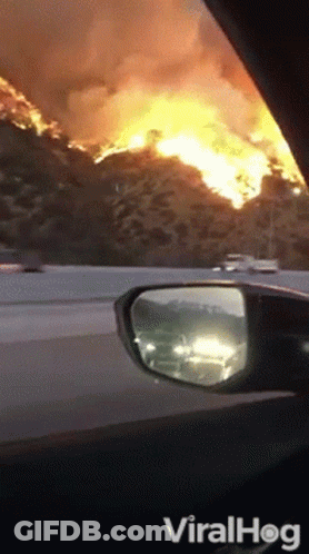 A Car Is Driving Down A Highway With A Large Fire In The Distance GIF