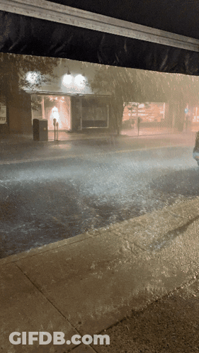 A Car Is Driving Down A Rainy Street In Front Of A Store GIF