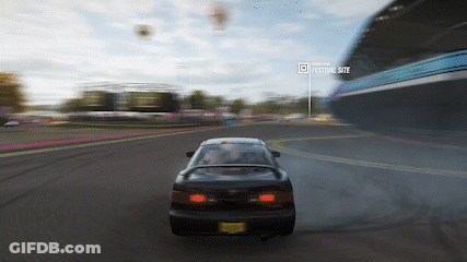A Car Is Driving Down A Road In Front Of A Festival Site GIF