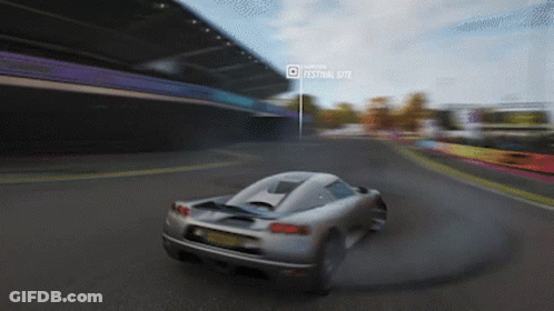 A Car Is Driving Down A Road In Front Of A Festival Site GIF