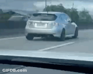A Car Is Driving Down A Road Next To A Parking Lot . GIF