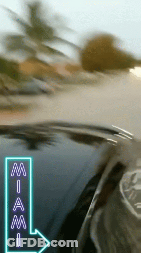 A Car Is Driving Down A Road With A Neon Sign Pointing To Miami GIF