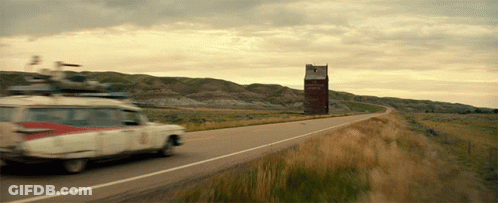 A Car Is Driving Down A Road With A Sign In The Background That Says ' Ghostbusters ' GIF