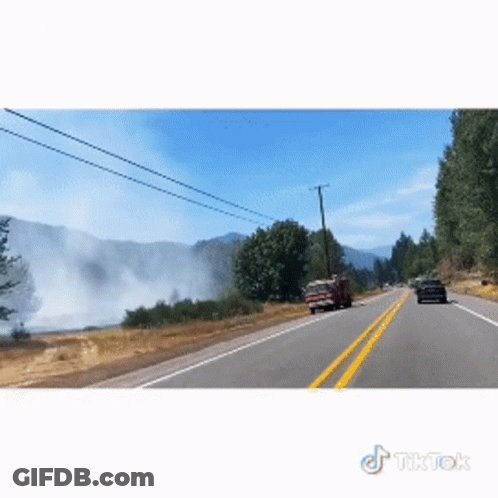 A Car Is Driving Down A Road With Smoke Coming Out Of The Mountains Behind It GIF