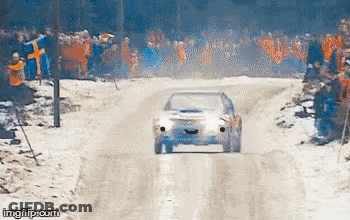 A Car Is Driving Down A Snow Covered Road In Front Of A Crowd . GIF