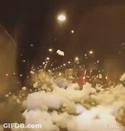 A Car Is Driving Down A Snowy Street At Night With A Lot Of Snow On The Ground . GIF