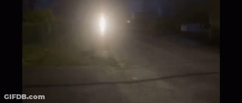 A Car Is Driving Down A Street At Night With A Bright Light Shining Through The Fog GIF
