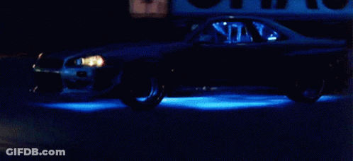 A Car Is Driving Down A Street At Night With Blue Lights On The Wheels GIF