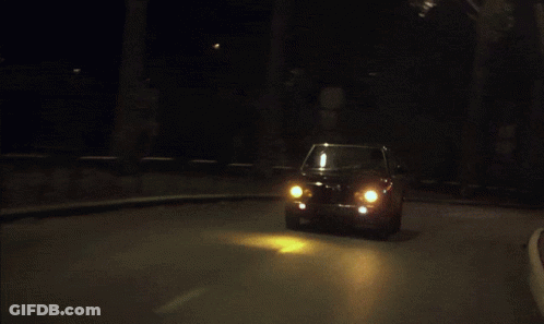 A Car Is Driving Down A Street At Night With The Lights On GIF