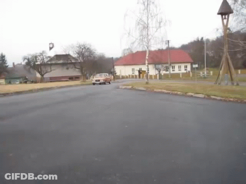 A Car Is Driving Down A Street In Front Of A Bell Tower GIF