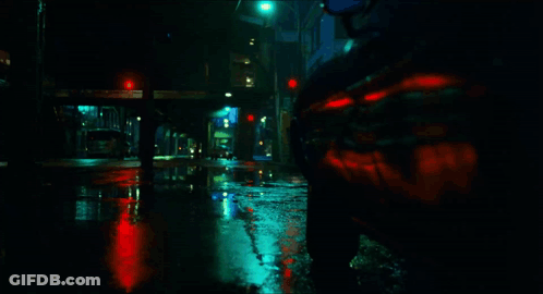A Car Is Driving Down A Wet Street With A Red Light In The Background GIF