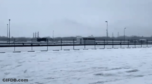 A Car Is Driving On A Snowy Road In A Parking Lot GIF