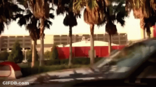 A Car Is Driving Past A Tent And Palm Trees In Front Of A Building GIF