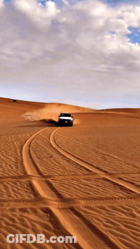 A Car Is Driving Through A Desert With A Cloudy Sky In The Background GIF