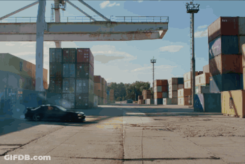 A Car Is Driving Through A Warehouse With Containers Stacked On Top Of Each Other And One Of The Containers Says Aa GIF