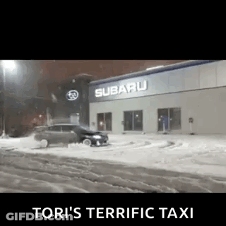 A Car Is Driving Through The Snow In Front Of A Subaru Car Dealership . GIF