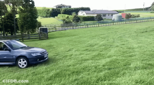 A Car Is Parked In A Grassy Field Next To A Fence . GIF