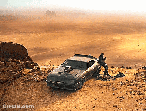 A Car Is Parked On A Dirt Hillside With A Man Standing Next To It And A Desert In The Background GIF