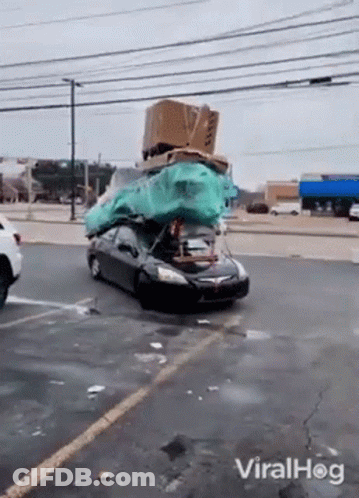 A Car With A Bunch Of Boxes On Top Of It Is Driving Down The Street . GIF