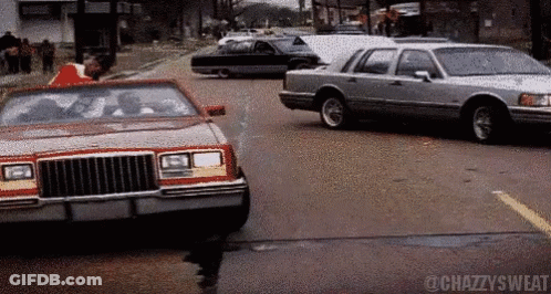 A Car With A Red Top Is Driving Down A Street Next To A Silver Car GIF