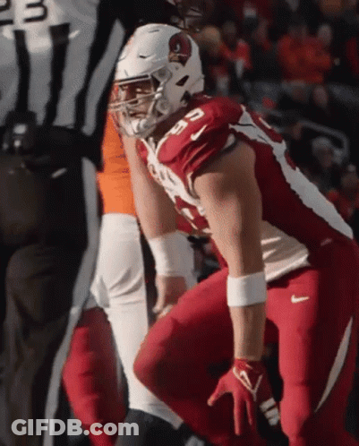 A Cardinals Football Player Squats Down In Front Of A Referee During A Game GIF