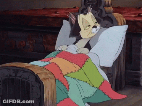 A Cartoon Cat Is Laying In A Bed With A Colorful Quilt GIF