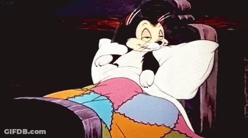 A Cartoon Cat Is Laying In A Bed With A Pillow GIF