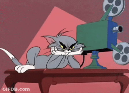 A Cartoon Cat Is Sitting At A Table Watching A Movie On A Film Camera . GIF