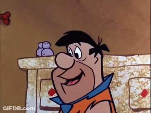 A Cartoon Character From The Flintstones Is Smiling While Standing In Front Of A Fireplace . GIF
