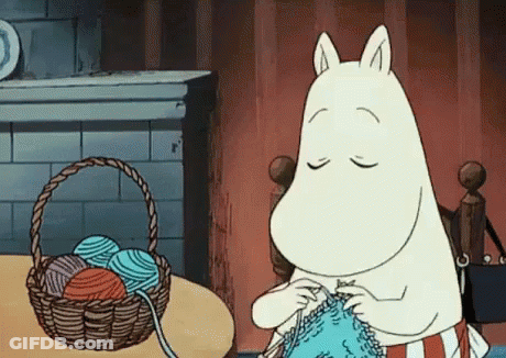 A Cartoon Character Is Knitting A Sweater In Front Of A Basket Of Yarn . GIF