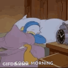A Cartoon Character Is Sleeping On A Bed Next To An Alarm Clock And Says `` Good Morning '' . GIF