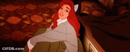 A Cartoon Girl With Red Hair Is Sitting On A Couch And Smiling . GIF