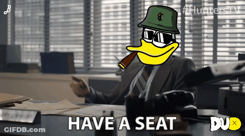 Man Sitting At Desk With Have A Seat Text GIF