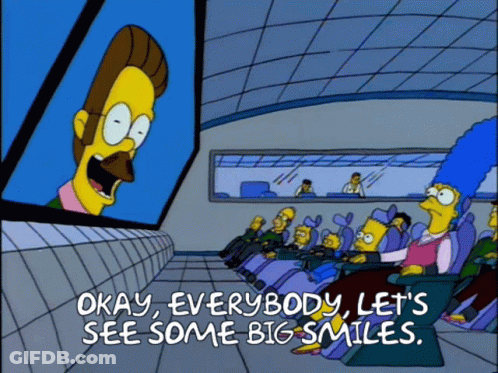 A Cartoon Says Okay Everybody Let 'S See Some Big Smiles In Front Of A Large Screen GIF