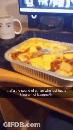 A Casserole Dish Of Lasagna With A Spoon In It On A Desk GIF