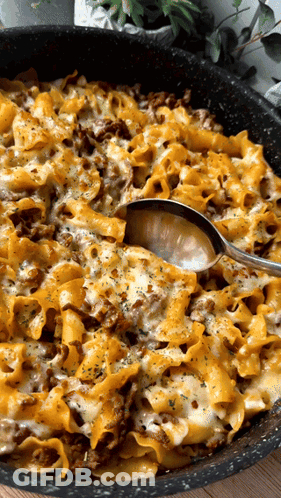 A Casserole Dish With Noodles And Cheese And A Spoon GIF